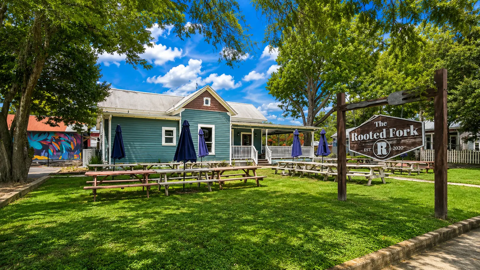 The Rooted Fork restaurant on Main Street in Cibolo, a blue cottage with picnic tables and a hand-painted sign out front